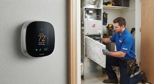 Modern high tech digital smart thermostat mounted on interior wall while technician replaces pleated HVAC filter
